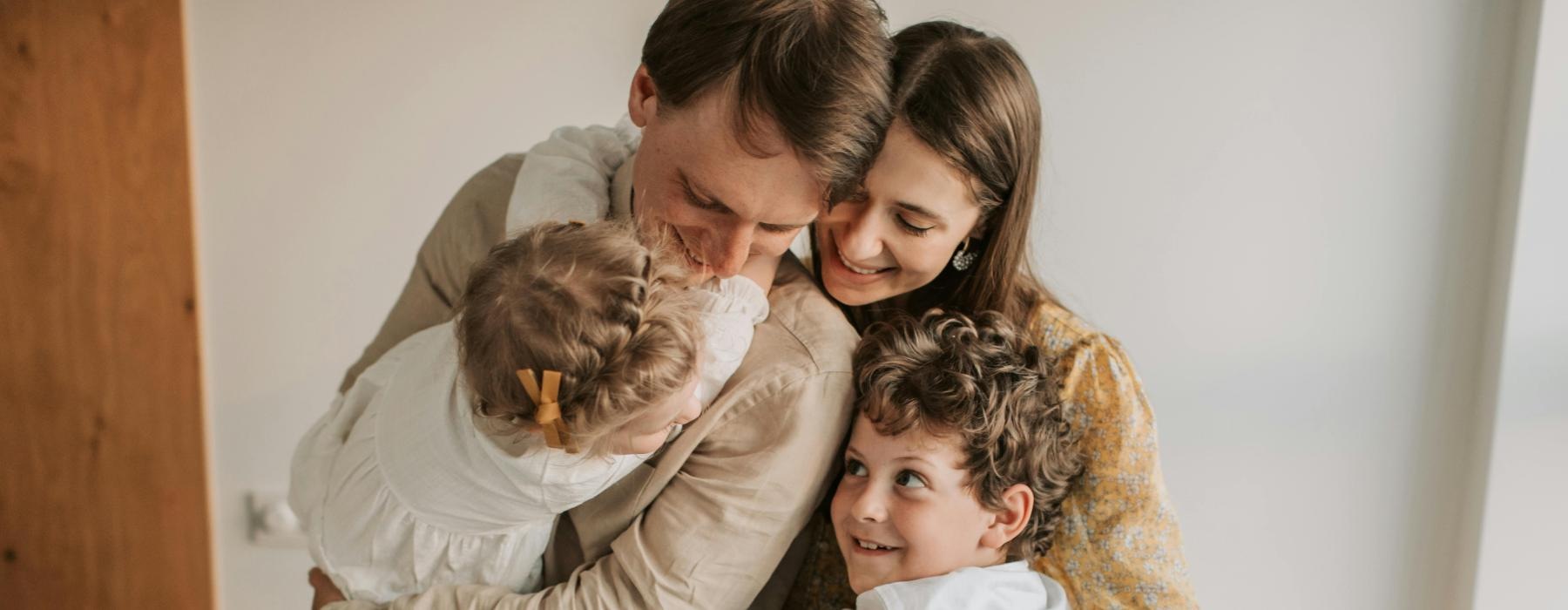 young family of four hugging in home