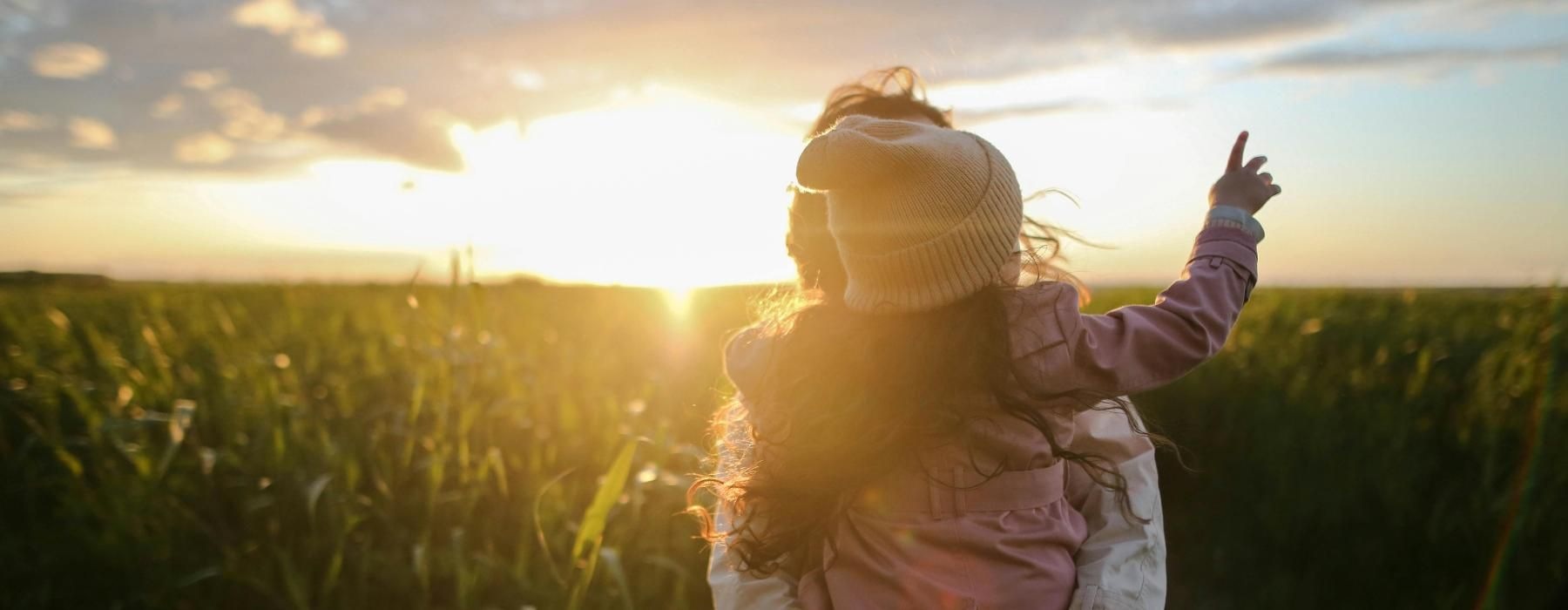 parent holding their child in a cornfield at sunset