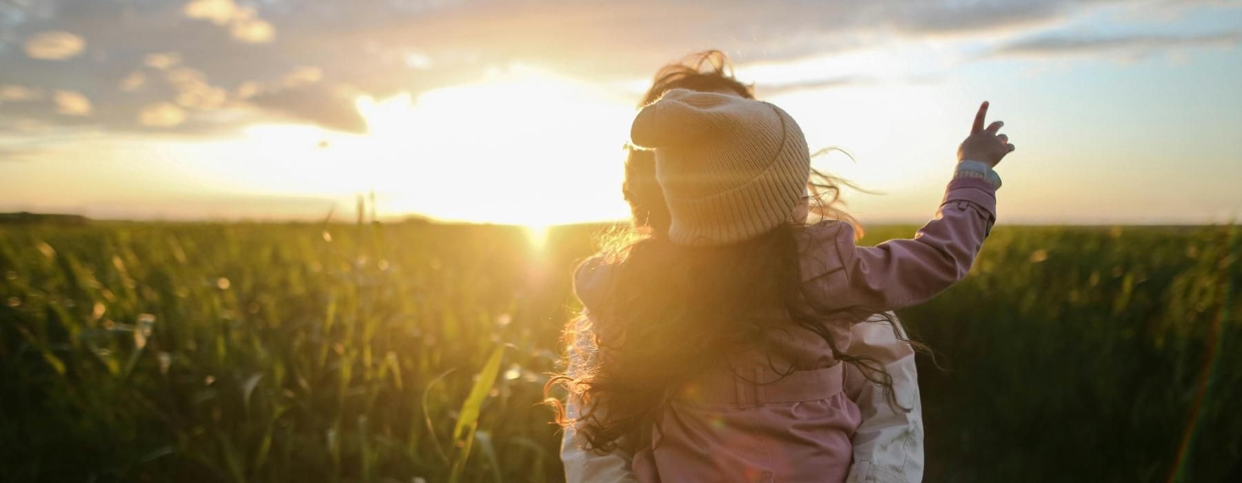 parent holding their child in a corn field at sunset